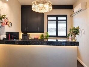 Una cocina moderna con armarios oscuros, encimera de mármol, lámpara de araña y ventana con persianas.