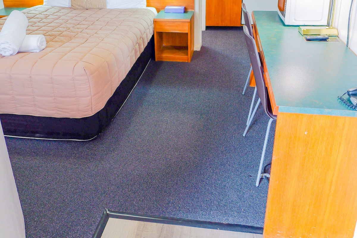 A hotel room with a bed, bedside tables, a desk, and a kitchenette.