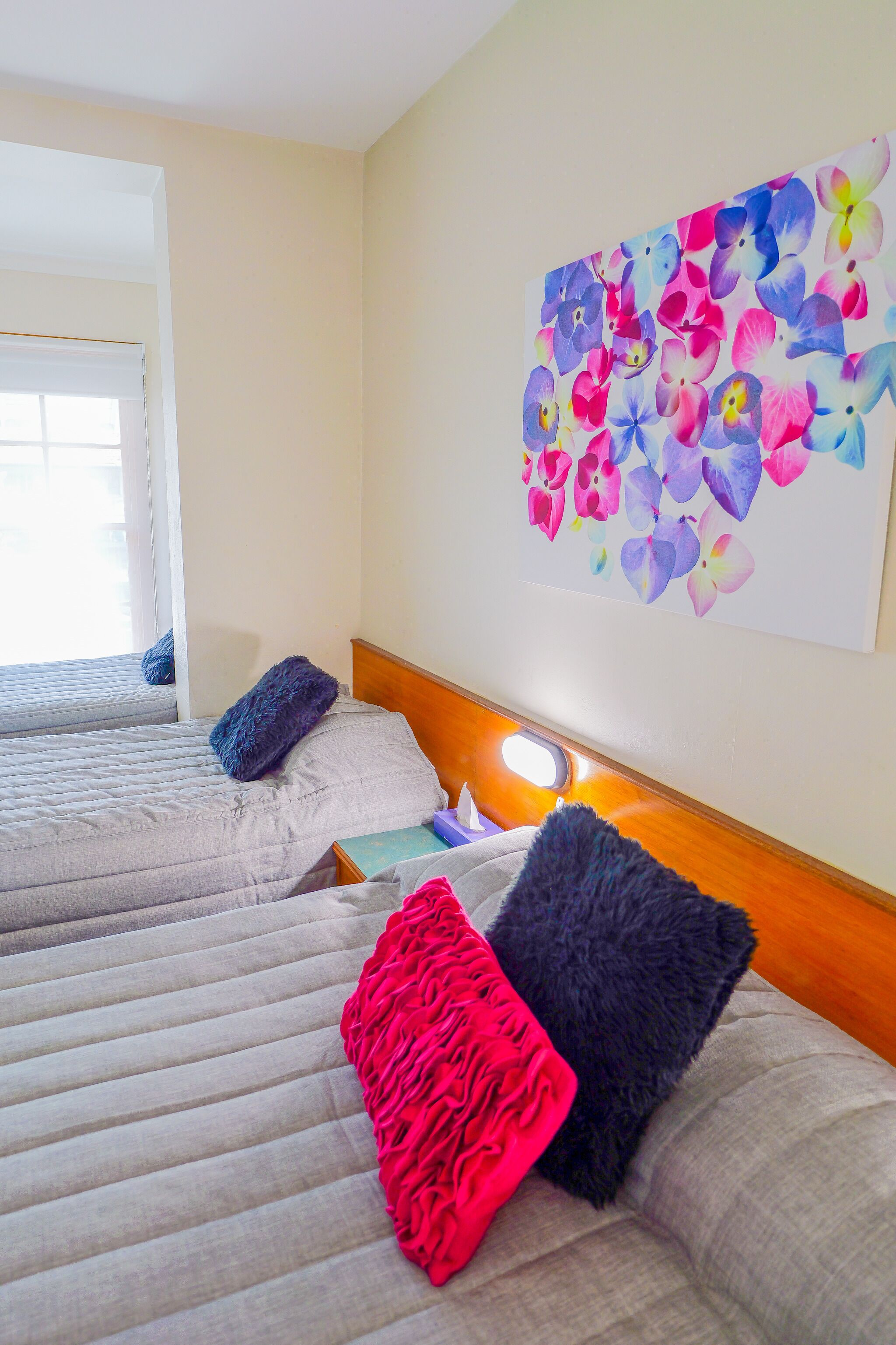 A hotel room with two beds, a large floral artwork on the wall, and a window with a view.