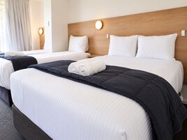 Habitación de hotel con dos camas, cabecero de madera y una ventana grande con cortinas.
