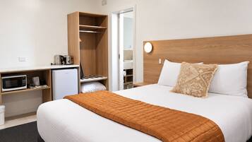 A hotel room with a bed, a desk with a microwave, a mini-fridge, and a wardrobe.