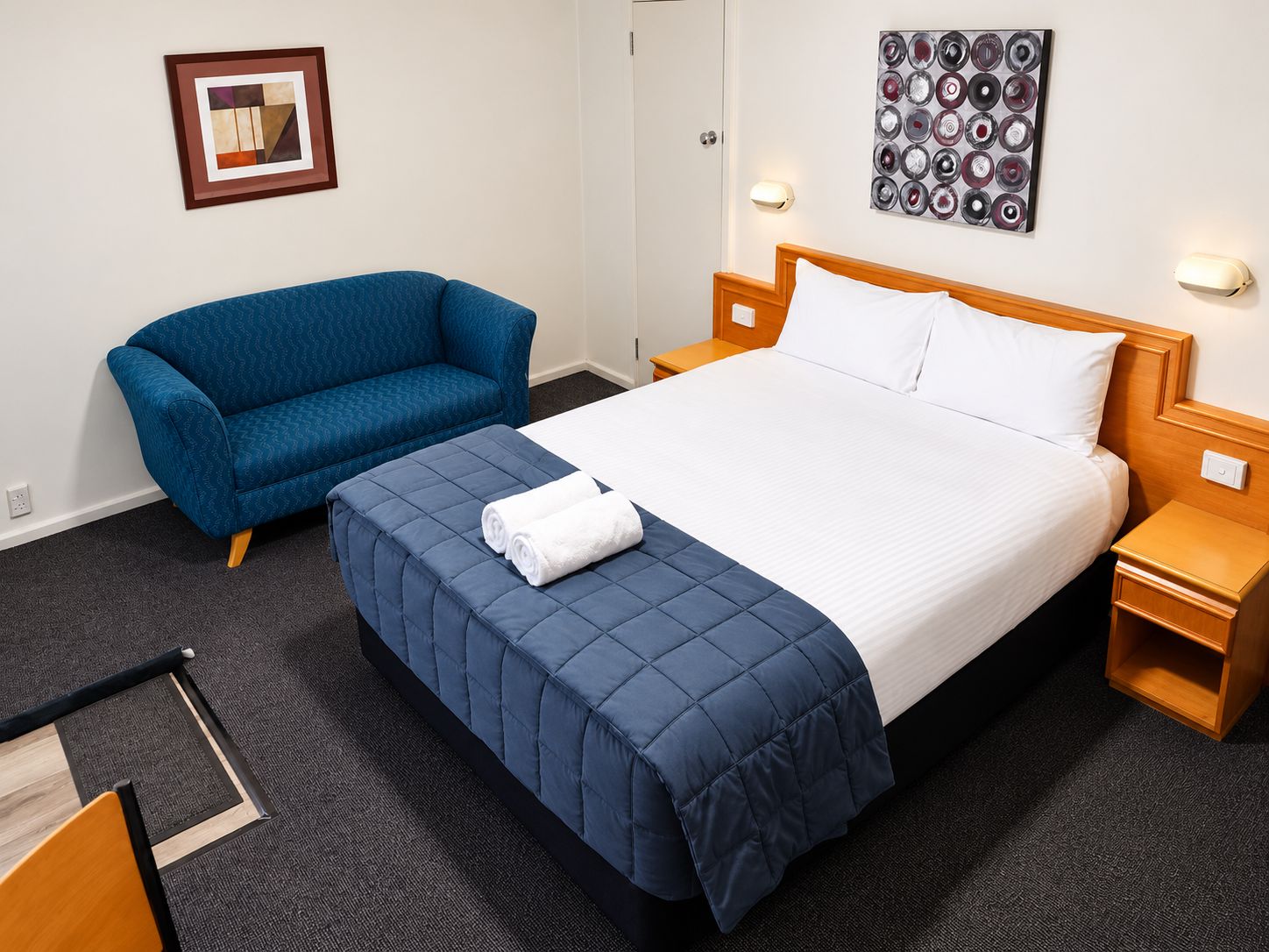 Una habitación de hotel con cama, sofá azul, una obra de arte en la pared y una mesita de noche.