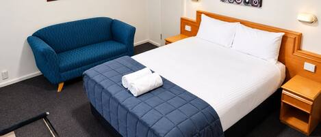 Una habitación de hotel con cama, sofá azul, una obra de arte en la pared y una mesita de noche.