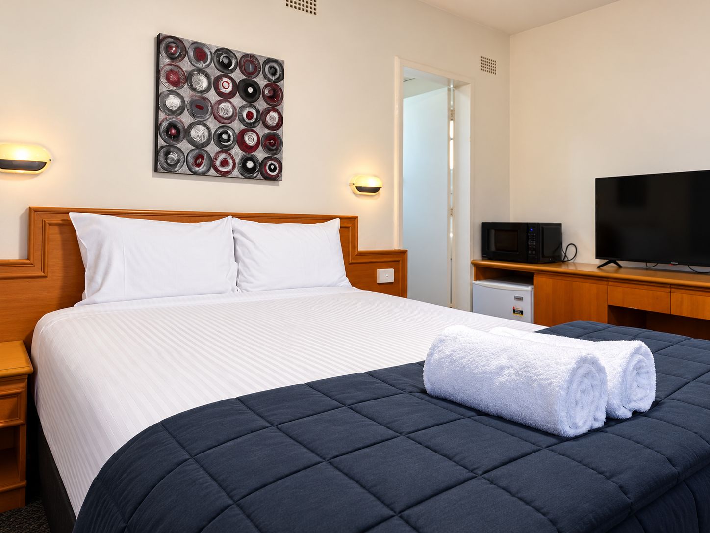 A hotel room with a bed, a television, a microwave, and a small refrigerator.
