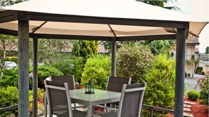 A covered outdoor seating area with a table and chairs, surrounded by greenery and a view of a residential street. - Abbotsleigh Motor Inn (Armidale)