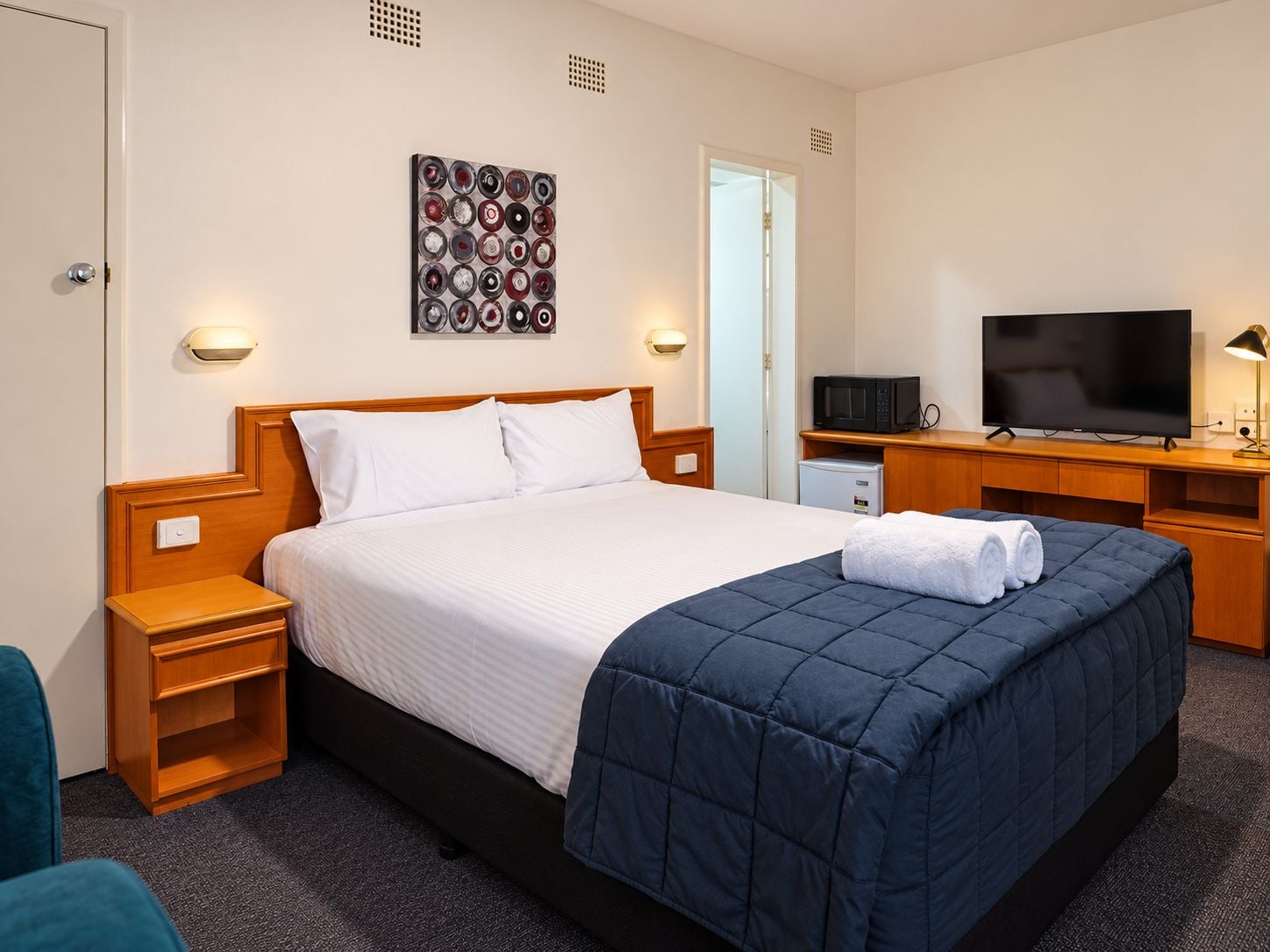 Quarto de hotel com cama, mesas de cabeceira, TV, micro-ondas e mini-geladeira.