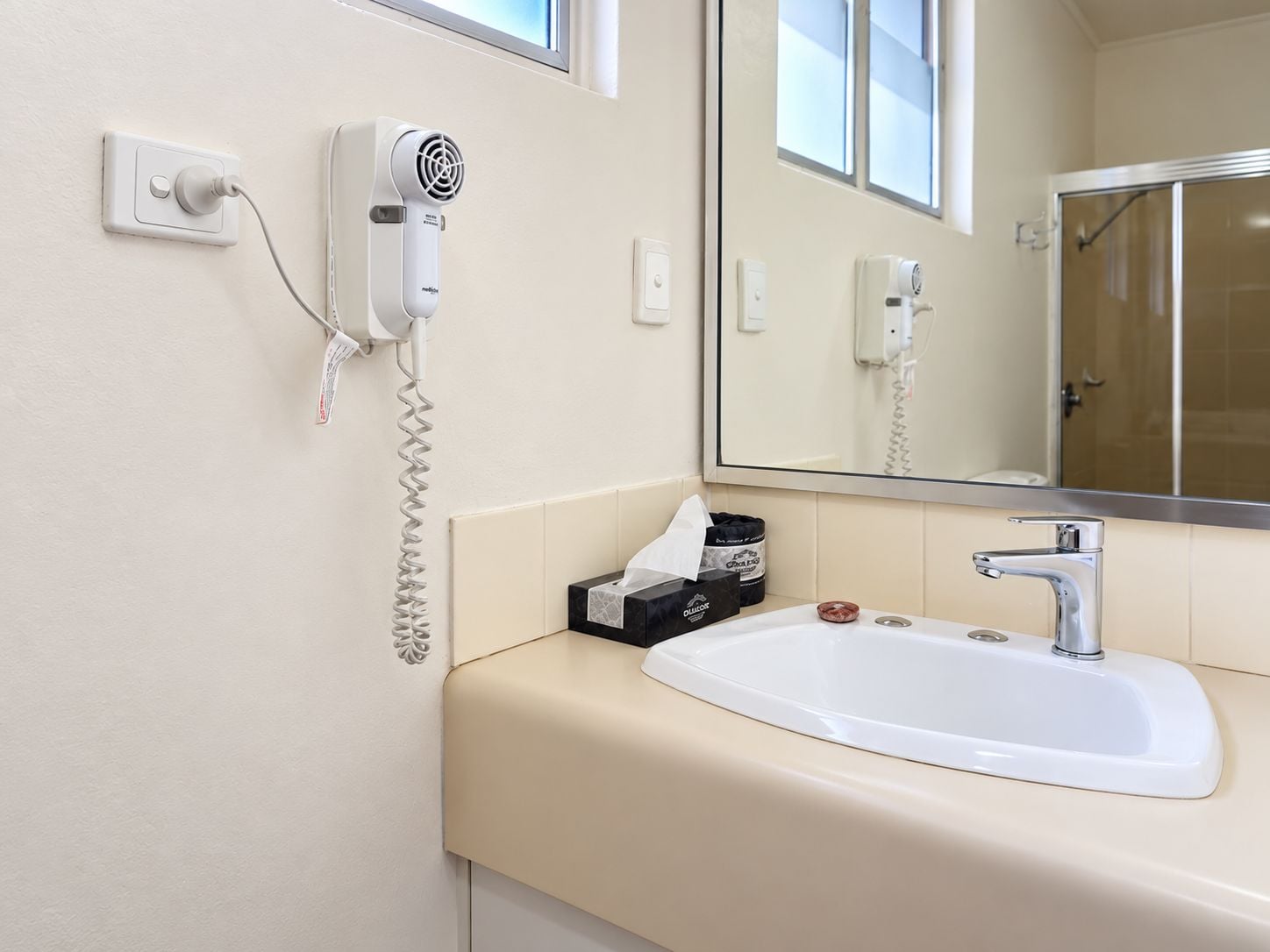 Ein Badezimmer in einem Hotel mit Waschbecken, Spiegel und Föhn an der Wand.
