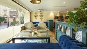 A hotel lobby with a blue sofa, a glass coffee table, and a view of the street outside. - Hotel Inglaterra Sevilla (Seville)