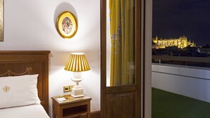 Habitación de hotel con cama, mesita de noche, lámpara, un cuadro enmarcado y vistas a un edificio iluminado.
