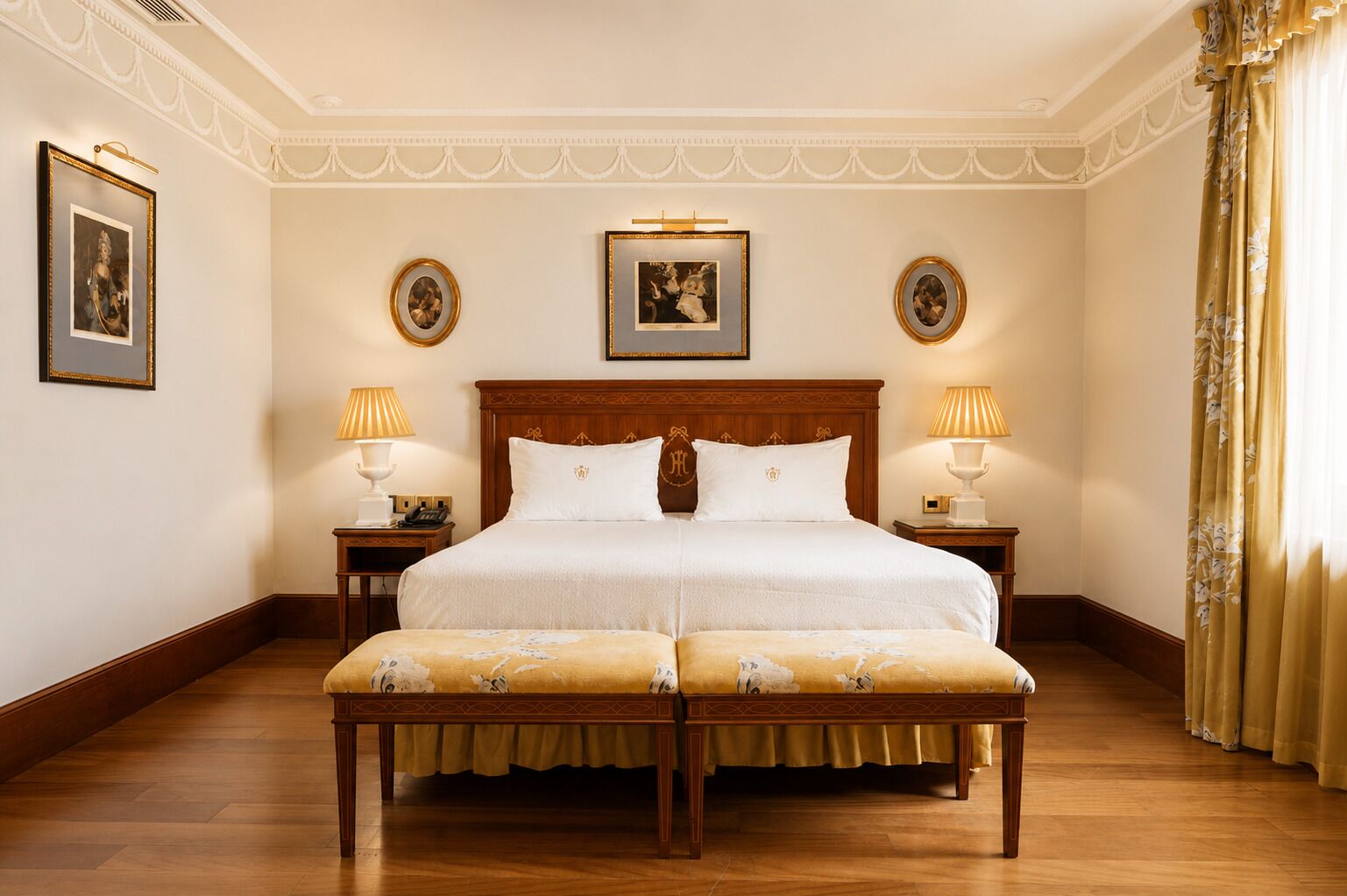 A spacious bedroom with a large bed, two bedside tables, a bench, and framed pictures on the walls.