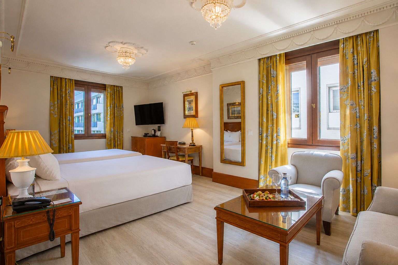 A hotel room with a large bed, a desk, a chair, a television, and a window with curtains.