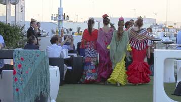 A rooftop event with people in colorful traditional dresses, outdoor seating, and a cityscape in the background.