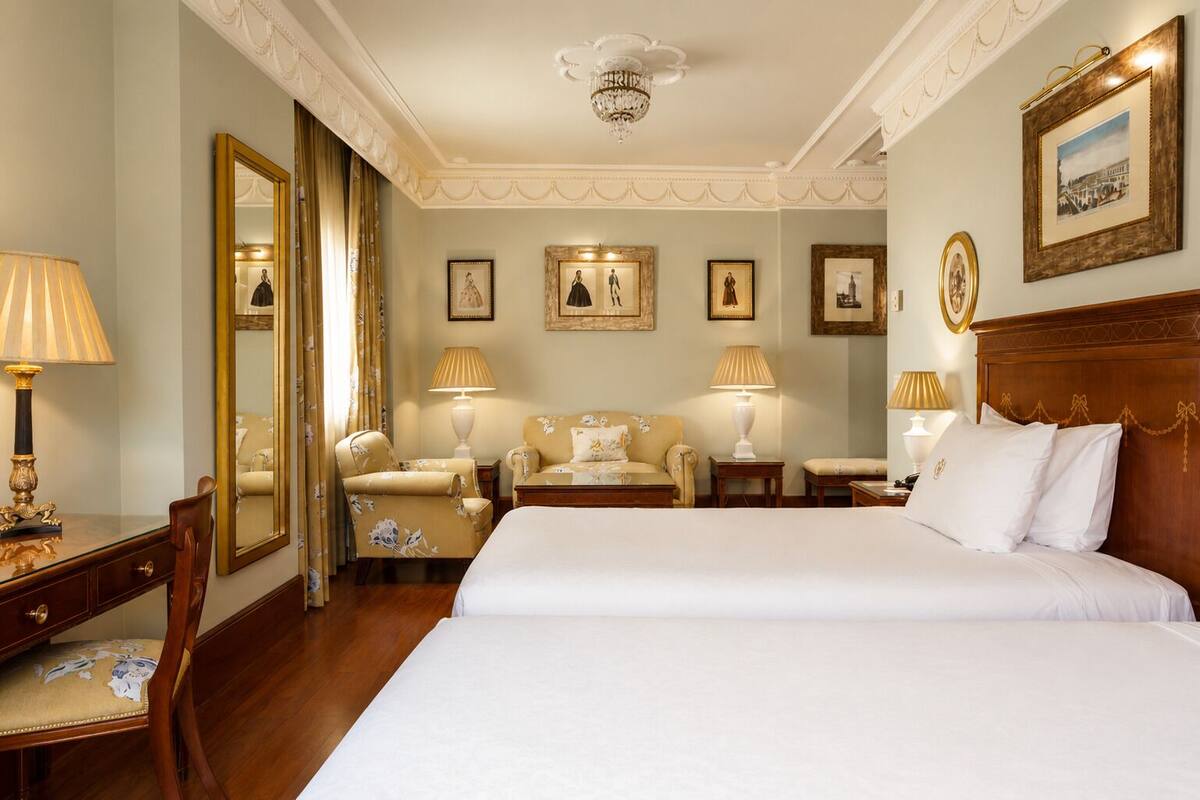 Habitación de hotel con una cama grande, dos mesitas de noche, un escritorio con silla, un espejo y cuadros en las paredes.
