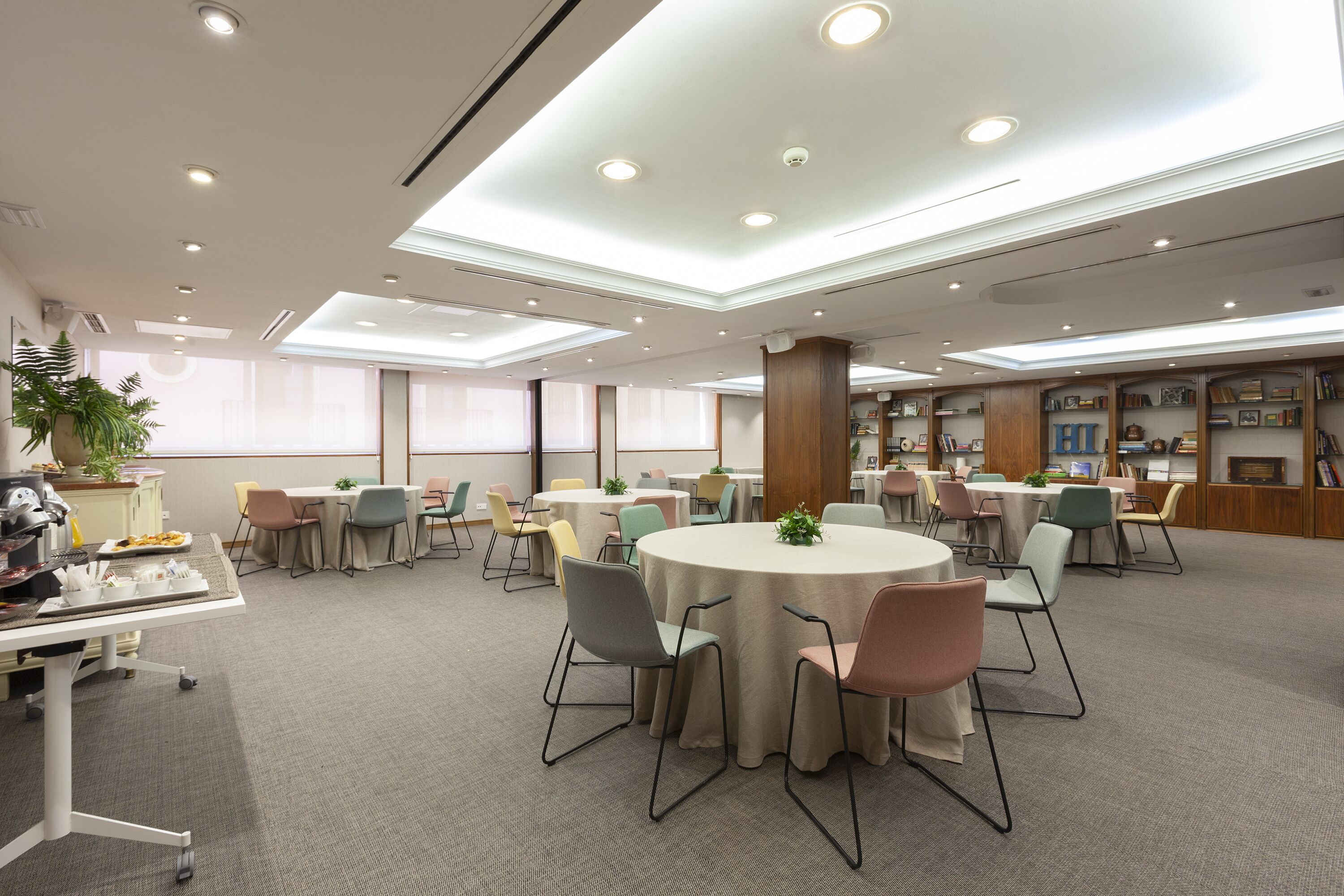 A spacious conference room with round tables, chairs, and a bookshelf filled with books.
