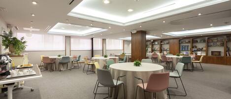 A spacious conference room with round tables, chairs, and a bookshelf filled with books.