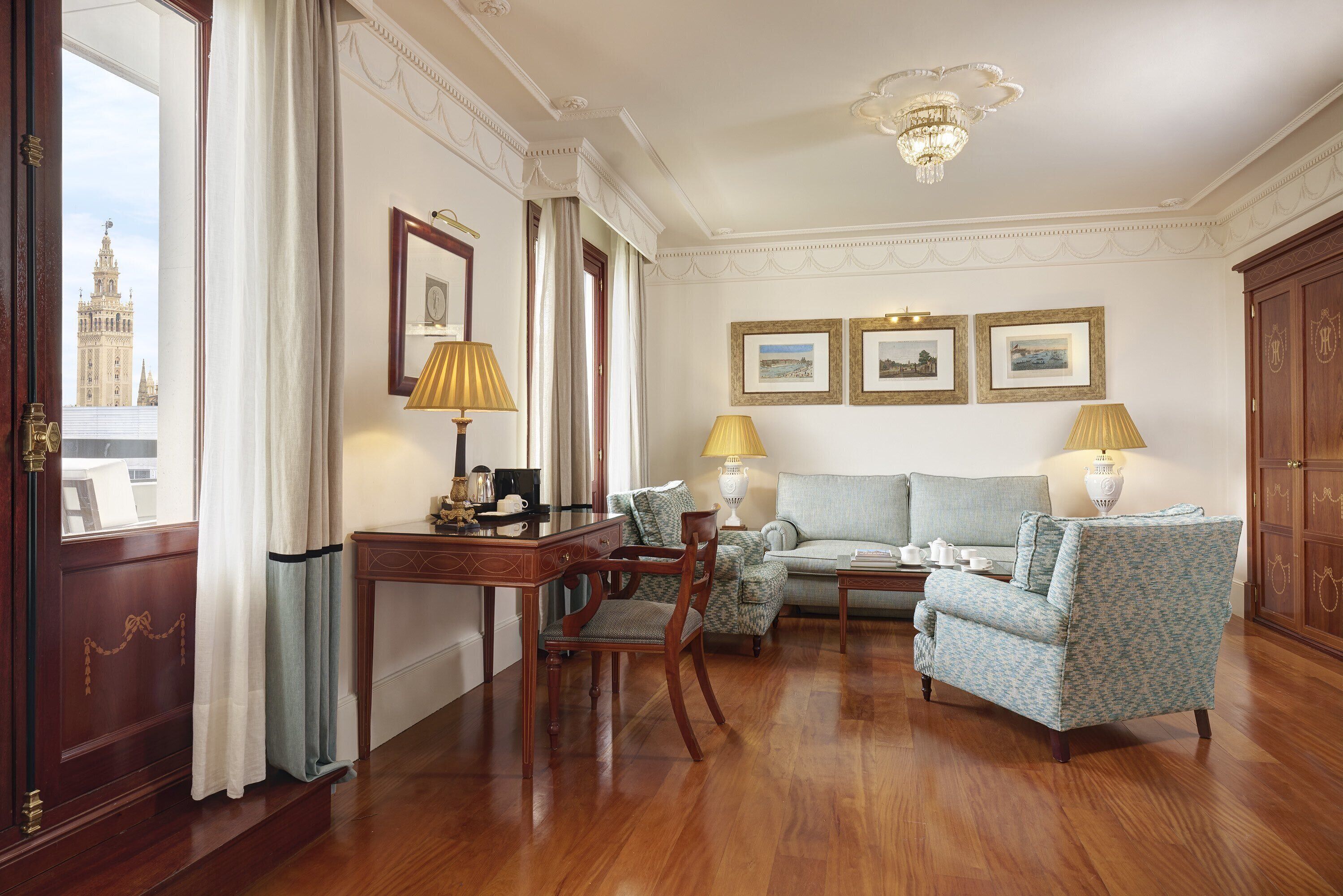 Una habitación con un escritorio de madera, dos sillones, un sofá y una araña.
