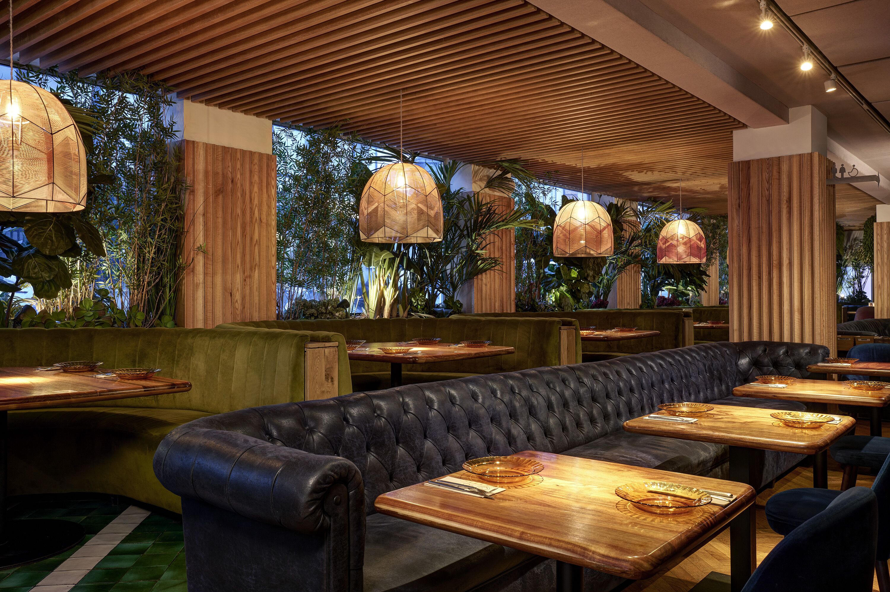 Interior de un restaurante con mesas de madera, asientos tipo banca de cuero y lámparas colgantes.