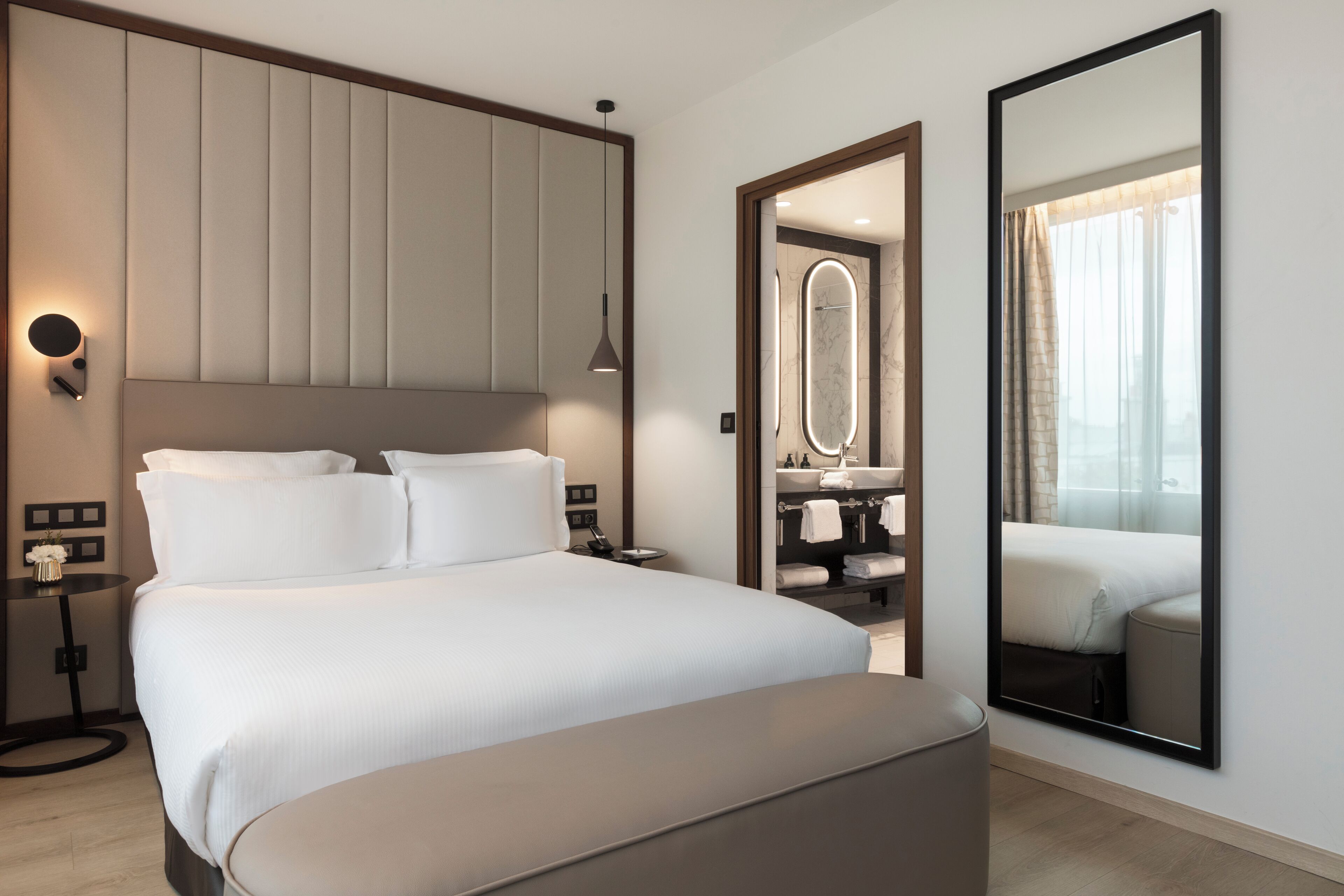 A modern hotel room with a large bed, bedside tables, a mirror, and a view of the bathroom.
