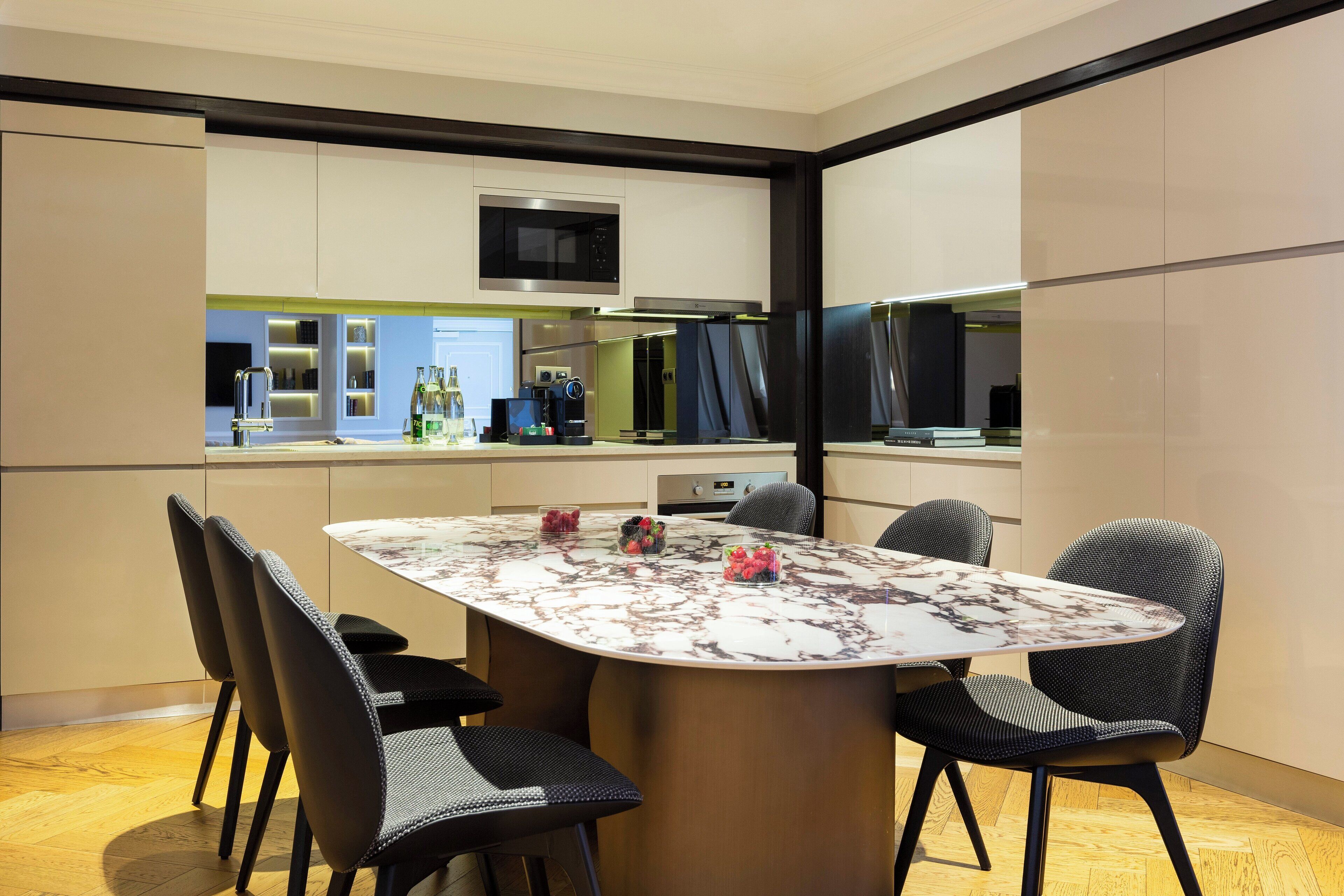 A modern kitchen with a built-in microwave, stove, and oven. There is a dining table with chairs and a bar area with a counter and stools.
