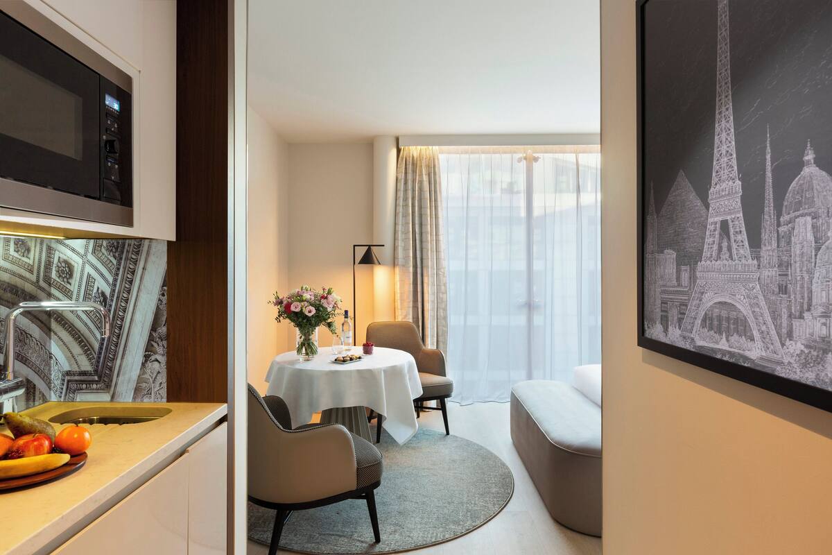 A hotel room with a dining area, a microwave, a sink, and a table with a vase of flowers.