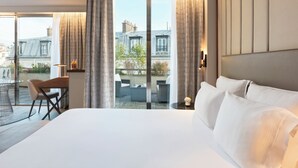 A hotel room with a large bed, a desk, and a view of the city through large windows. - La Clef Tour Eiffel Paris by The Crest Collection (Paris)