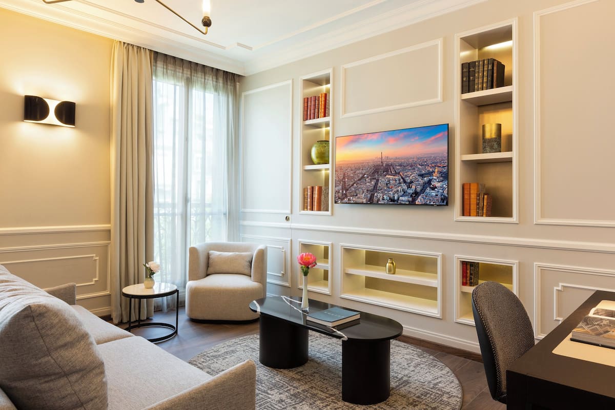A modern living room with a sofa, armchair, coffee table, and built-in bookshelves with a cityscape painting.