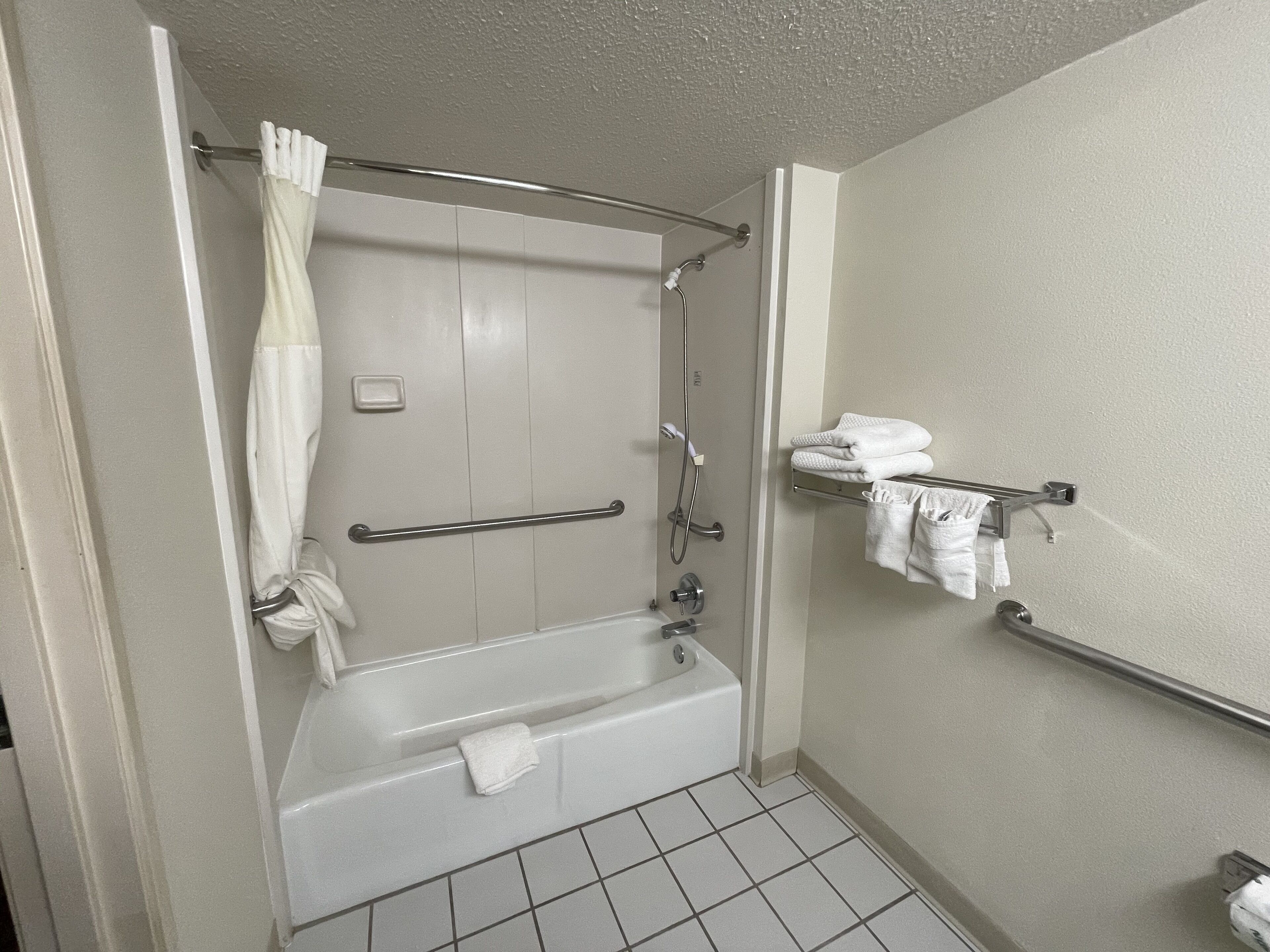 A bathroom with a bathtub, a shower, a handrail, and a towel rack.