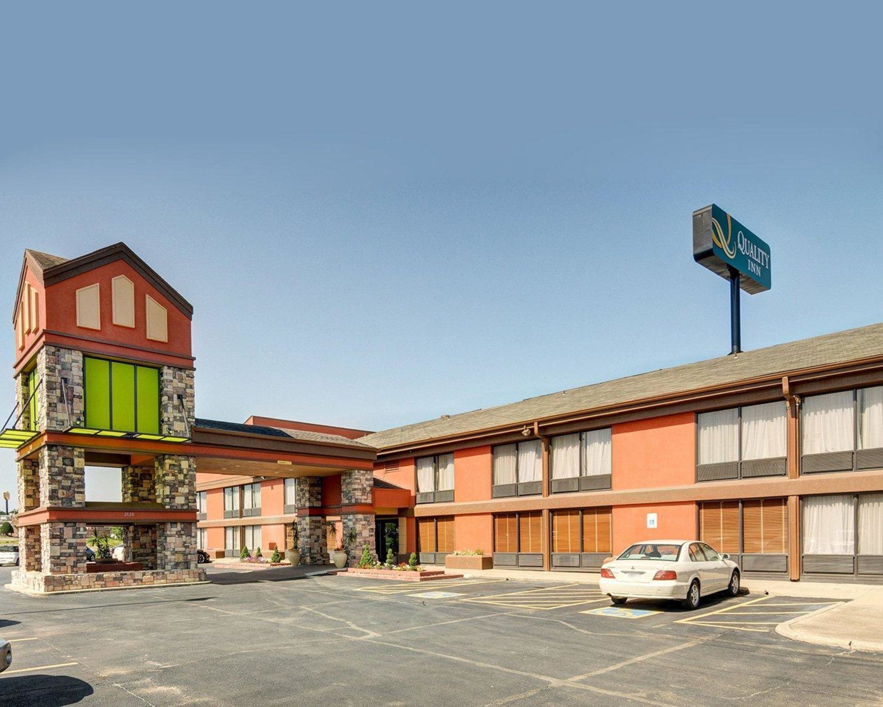 A hotel with a distinctive stone and glass entrance, a parking lot, and a sign indicating it is a Quality Inn.