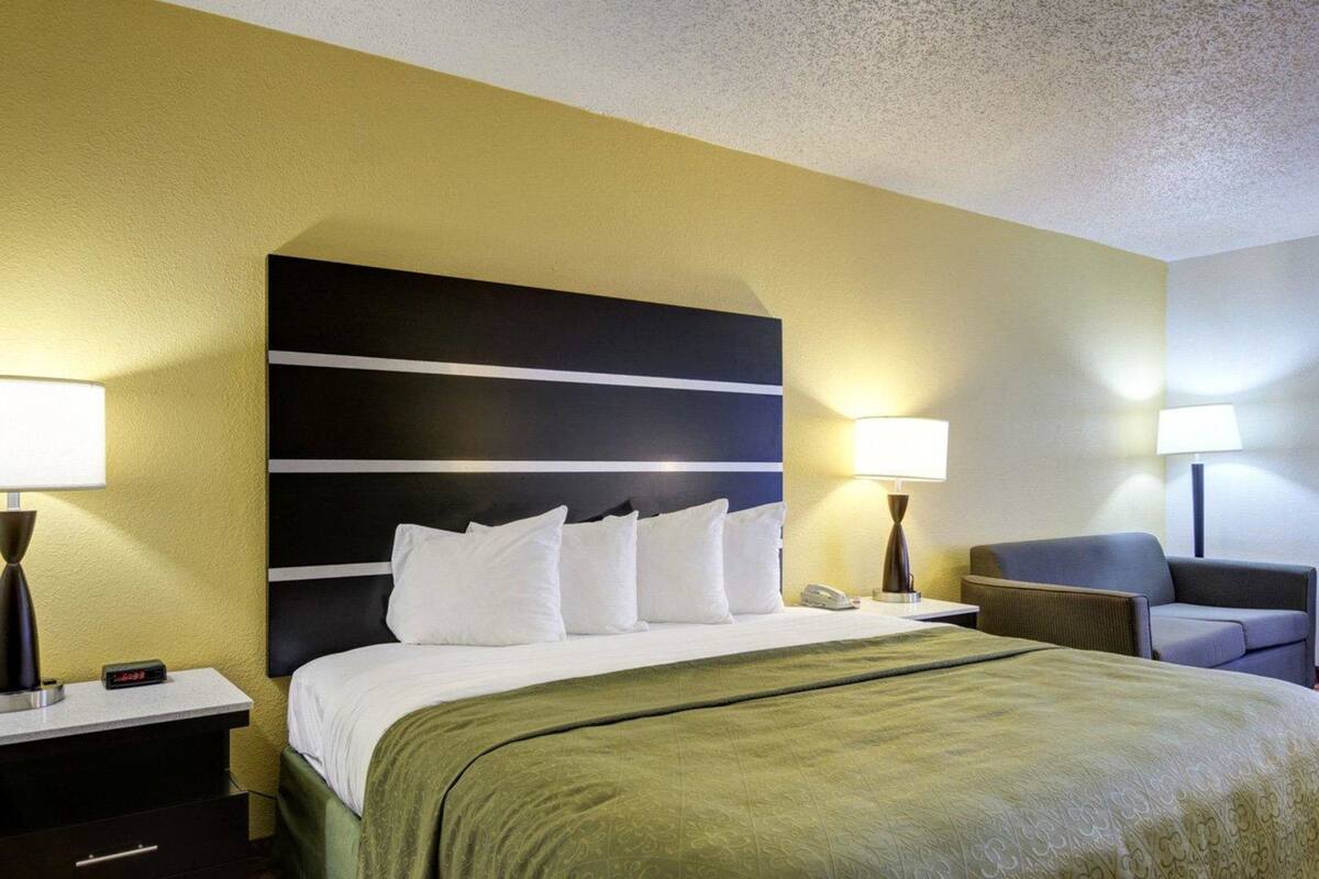 A hotel room with a large bed, two bedside tables, a nightstand, a chair, and a lamp.