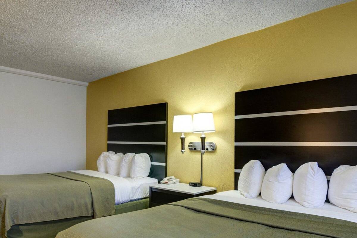 A hotel room with two beds, each with white linens and pillows, a bedside table with a lamp, and a phone.