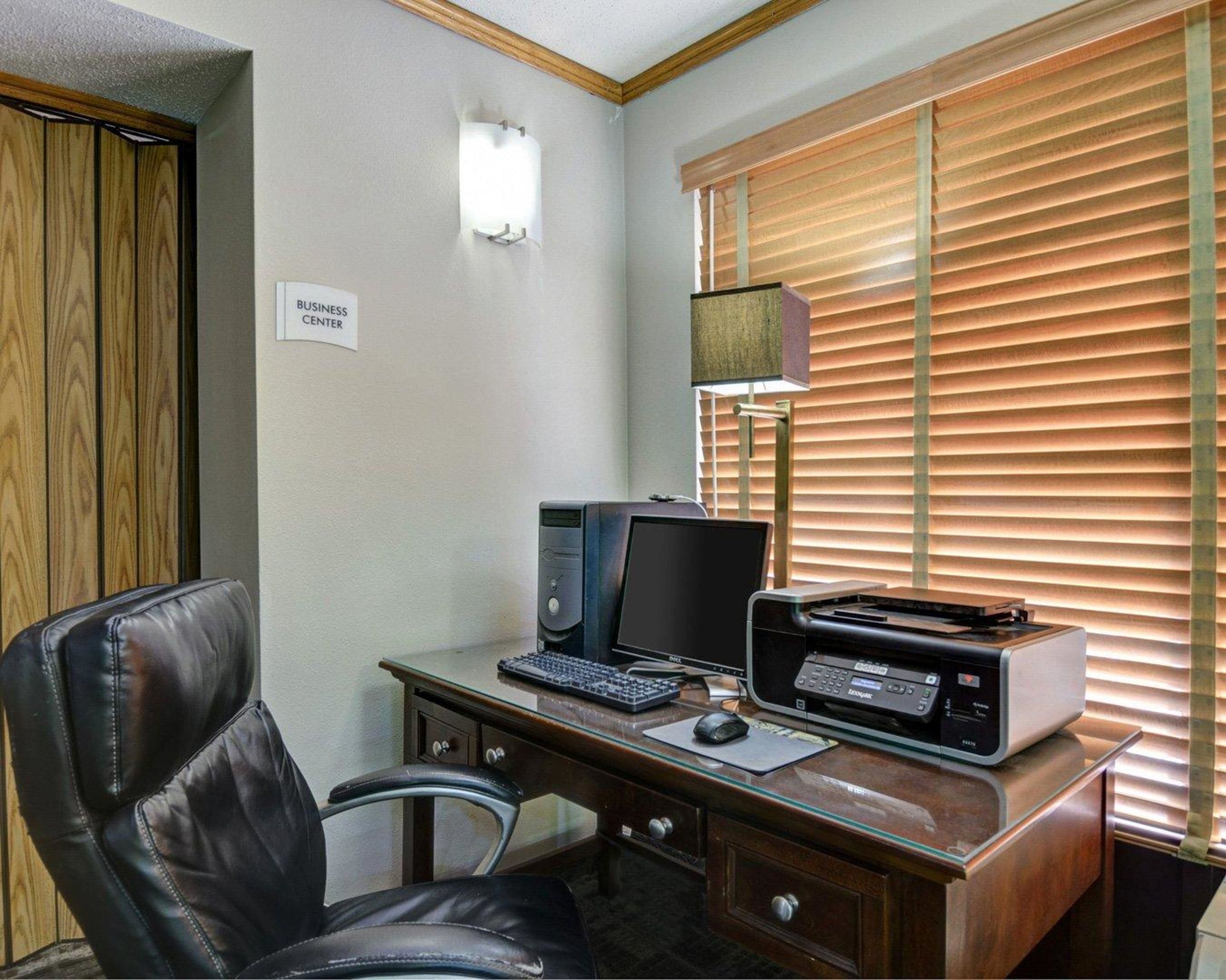 A business center with a desk, computer, printer, and a chair.