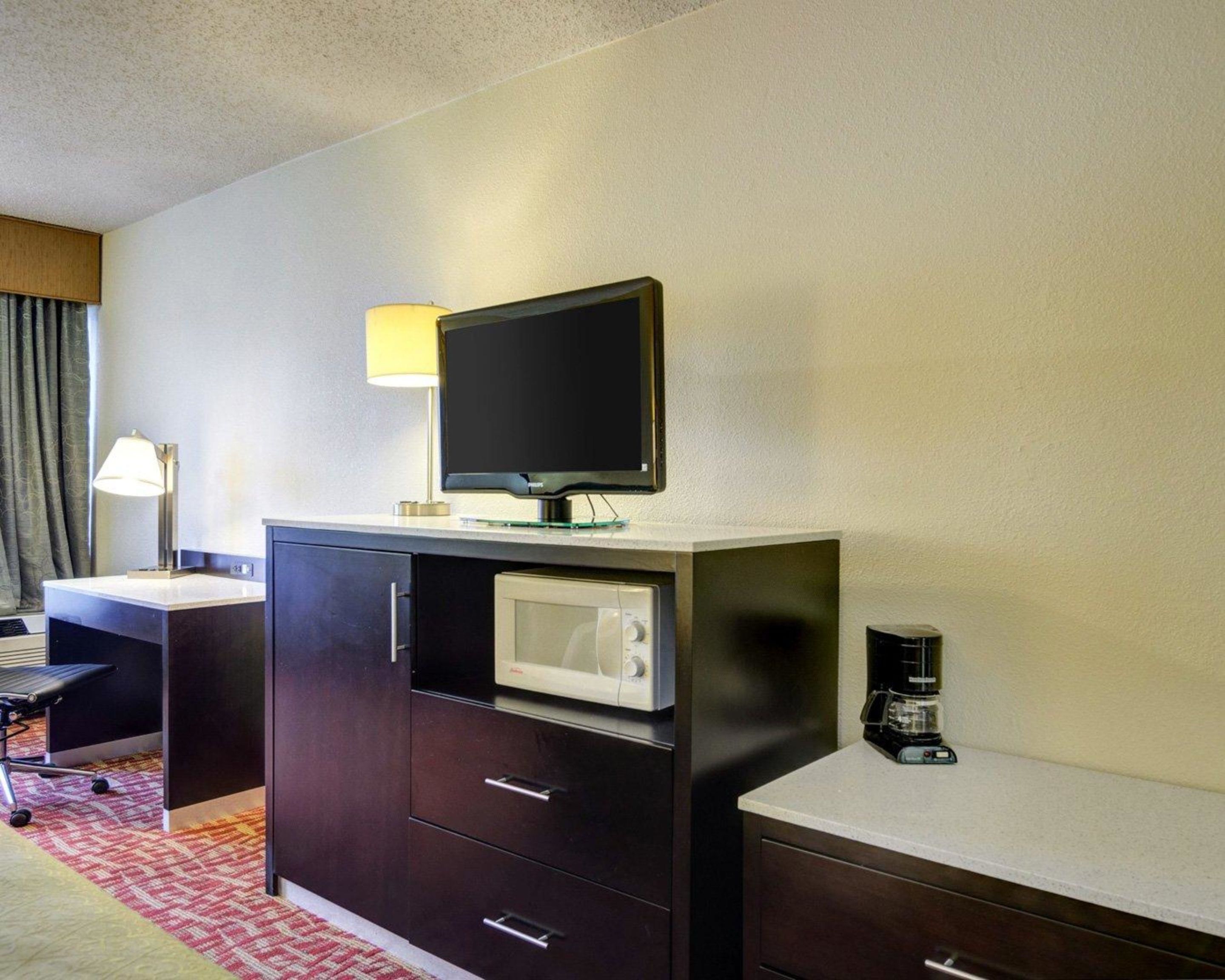 Habitación de hotel con escritorio, televisor de pantalla plana, microondas, cafetera y lámpara.