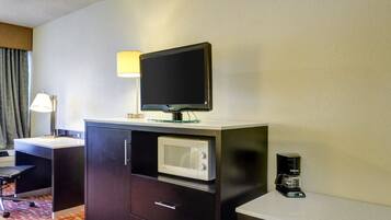A hotel room with a desk, a flat-screen TV, a microwave, a coffee maker, and a lamp.
