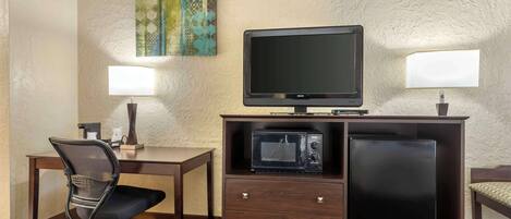 Habitación de hotel con escritorio, silla, televisión, microondas, refrigerador y dos lámparas de pared.
