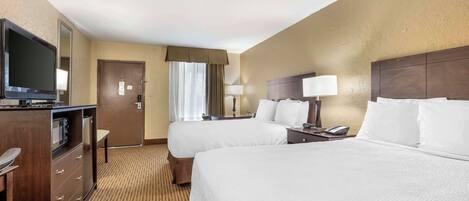 A hotel room with two beds, a TV, a desk, and a minibar.