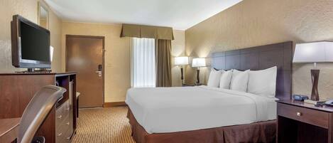 A hotel room with a large bed, a desk with a television, a chair, and a door.