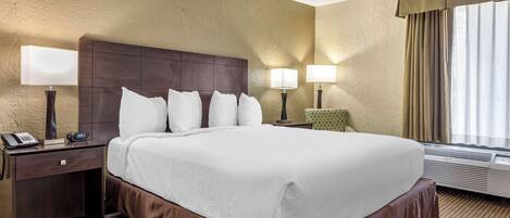 A hotel room with a large bed, two bedside lamps, a nightstand with a phone, and a window with curtains.
