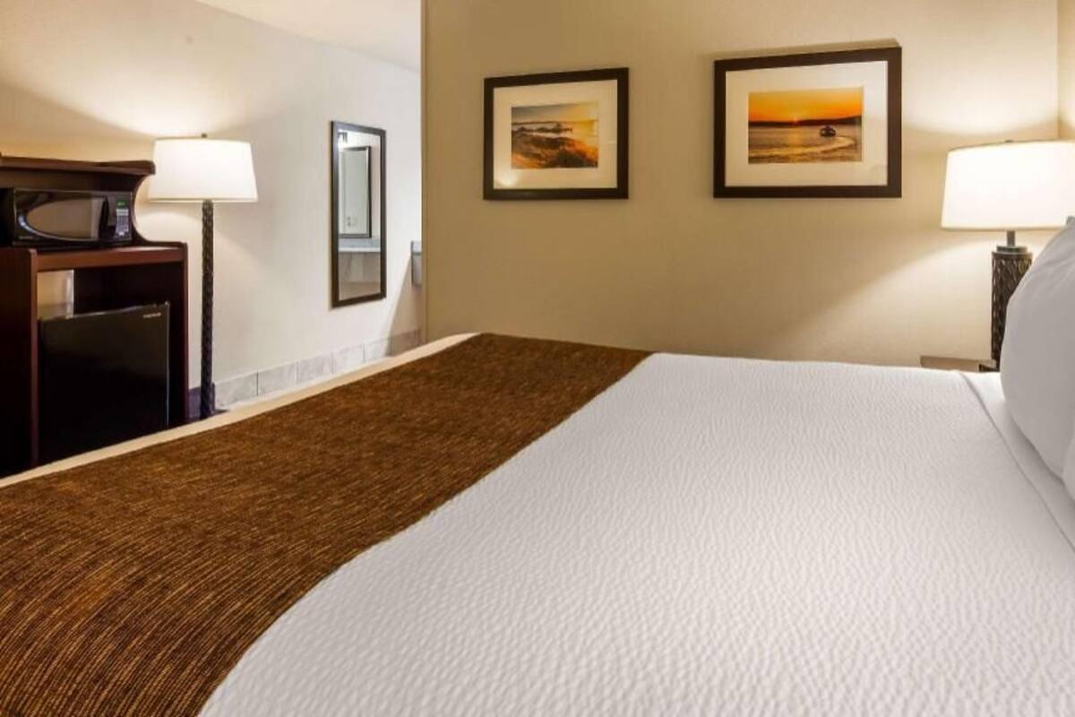 Een hotelkamer met een bed, twee ingelijste foto's aan de muur, een bureau met een lamp en een magnetron.