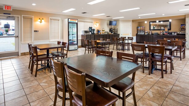 A hotel dining area with multiple tables and chairs, a refrigerator with beverages, and a coffee station. - Best Western Lakewood (Lakewood)