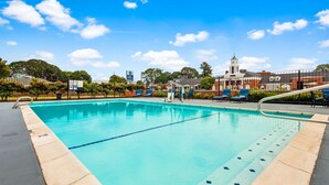 A clear blue swimming pool with a lifeguard stand, lounge chairs, and a fenced area with a building in the background. - Best Western Lakewood (Lakewood)
