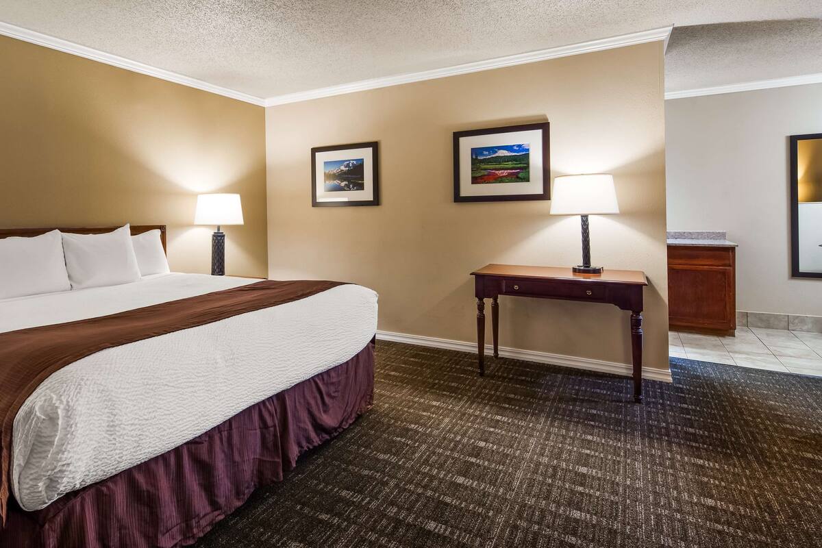 Een hotelkamer met een groot bed, twee bedlampjes, een klein tafeltje en twee foto's in lijsten aan de muur.