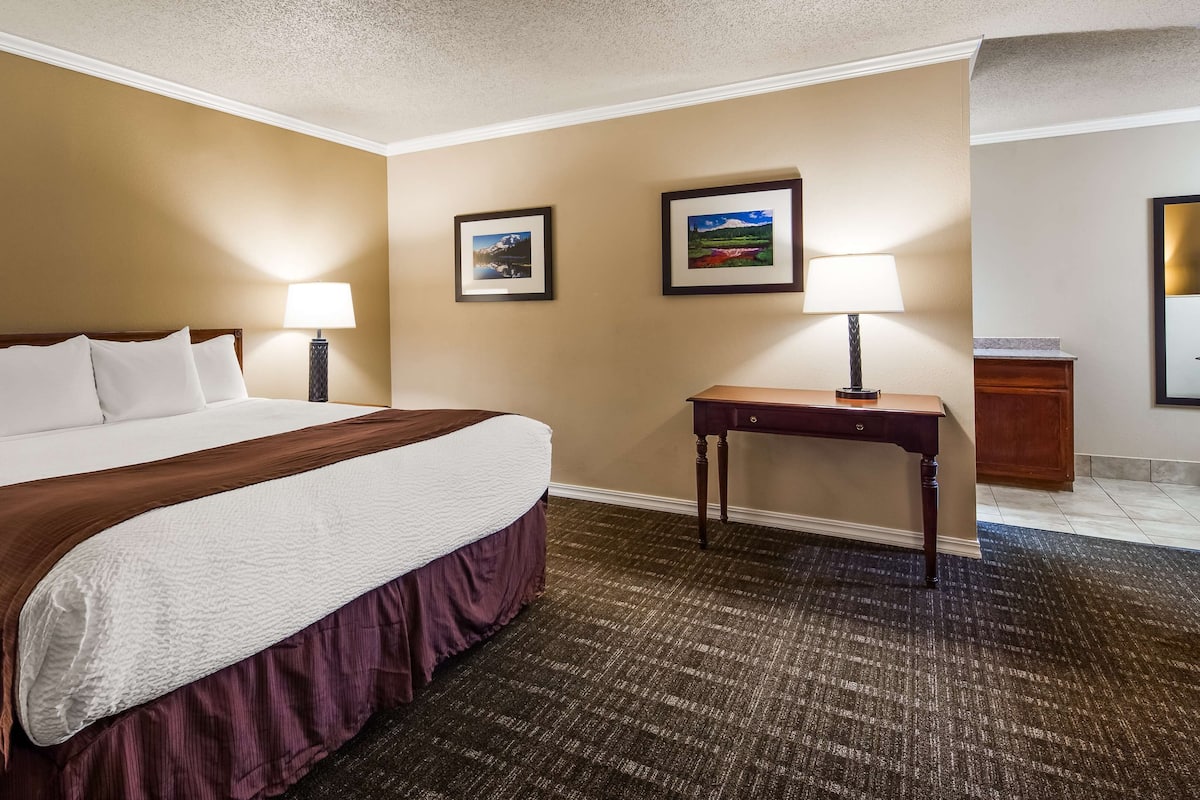 Quarto de hotel com uma cama grande, duas luminárias de cabeceira, uma mesinha e duas quadros na parede.
