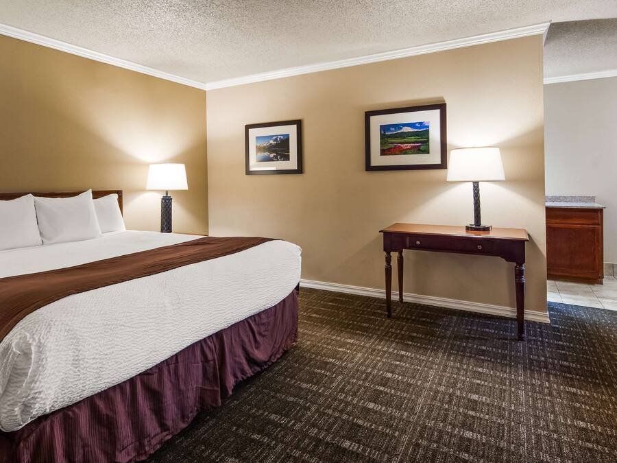 Een hotelkamer met een groot bed, twee bedlampjes, een klein tafeltje en twee foto's in lijsten aan de muur.