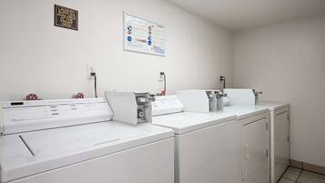 A laundry facility with three front-loading washers and dryers, a price tag, and a laundry care poster on the wall.