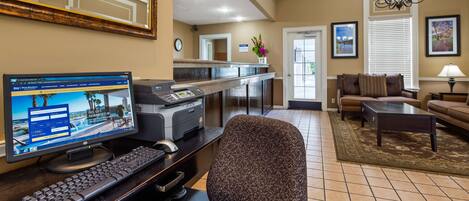 Un hall de hotel con mostrador de recepción, computadora y zona de estar.