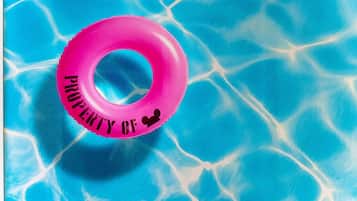 A pink inflatable ring with the text "PROPERTY OF" in a swimming pool.