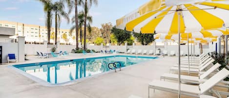 A swimming pool with lounge chairs and yellow and white striped umbrellas.