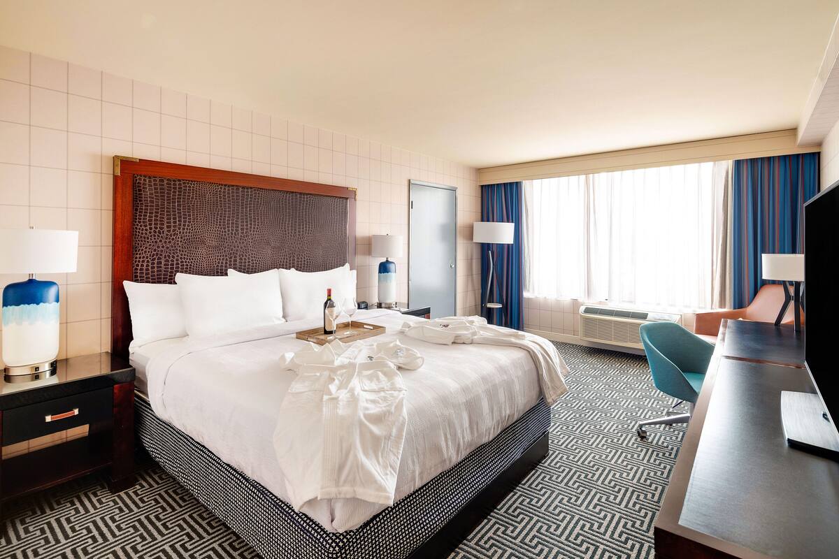 A hotel room with a large bed, a desk, a chair, and a TV.
