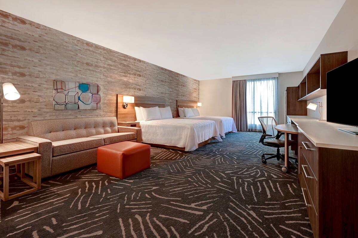 A hotel room with a large bed, a sofa, a desk, and a TV.