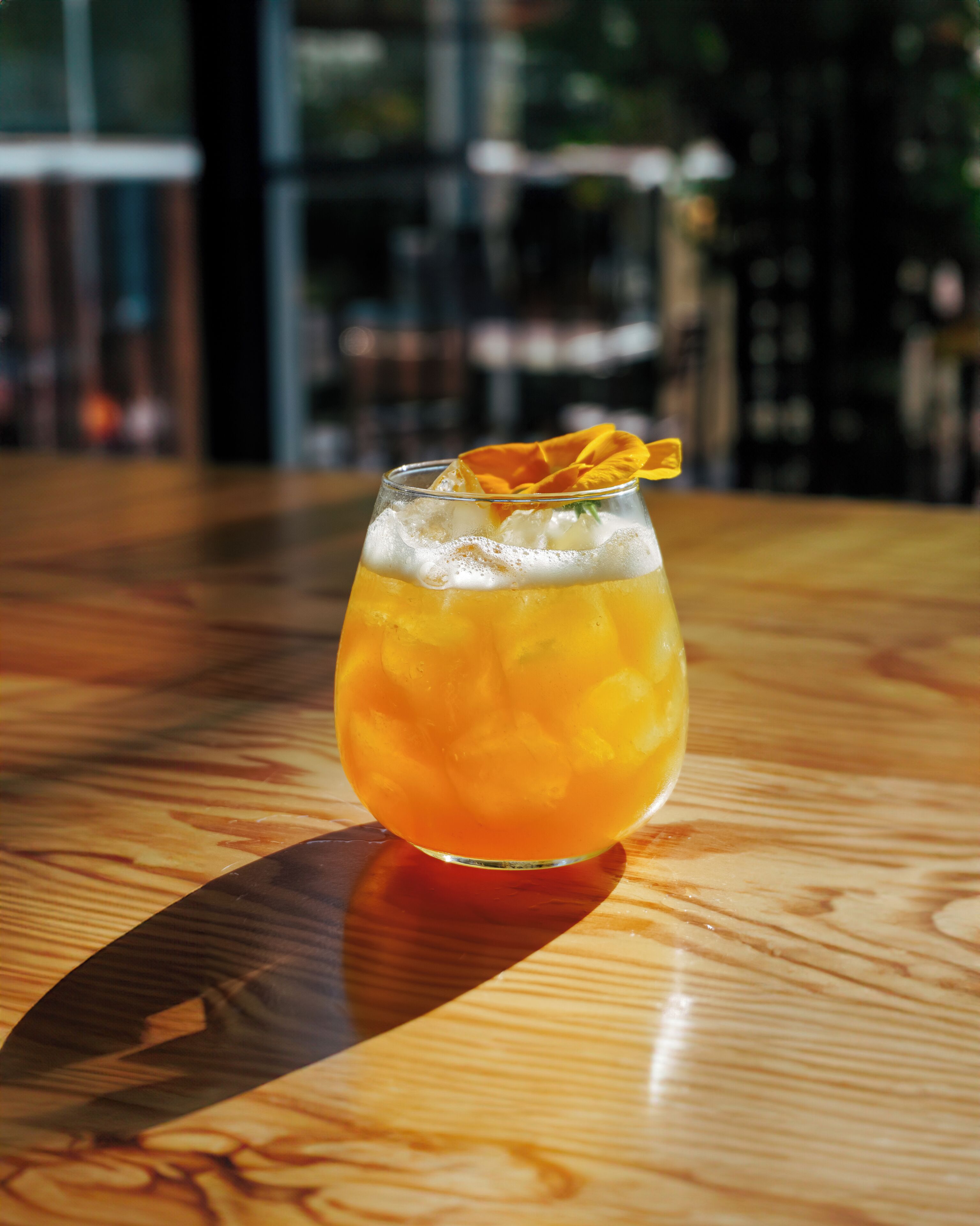 Un vaso de bebida color ámbar con cubitos de hielo y una guarnición sobre una mesa de madera.